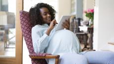 Pregnant person sitting in a chair looking at a tablet