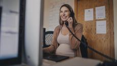 Pregnant person sitting at a desk talking on the phone while looking at a computer