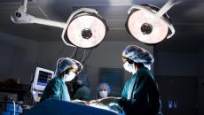 Surgeons in an operating room standing above a patient on a table with large lights above them