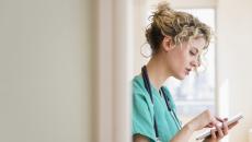 Healthcare provider in green scrubs wearing a stethoscope around their neck while looking at a tablet