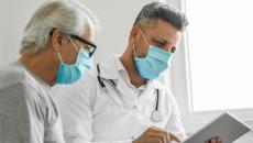 Patient and doctor in masks looking at tablet