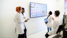 A group of researchers looking at data on a television screen.