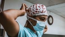 A health worker wearing a surgical mask ties their head cap
