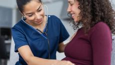 Healthcare professional listening to a pregnant person's stomach with a stethoscope