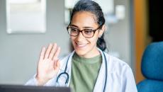Healthcare provider sitting in front of a computer waving at the screen