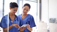 Healthcare providers standing next to each other while wearing blue scrubs and looking at a tablet