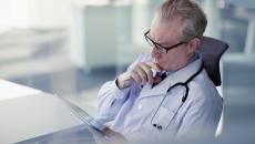 Healthcare provider looking at a tablet while holding their chin as though deep in thought