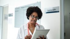 Healthcare provider wearing a lab coat and a stethoscope looking at a tablet