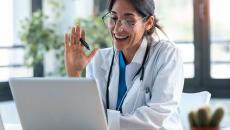 Healthcare provider sitting at a desk and looking at a computer while waving to the screen