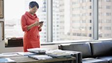 A woman standing at her desk looking down at her smartphone